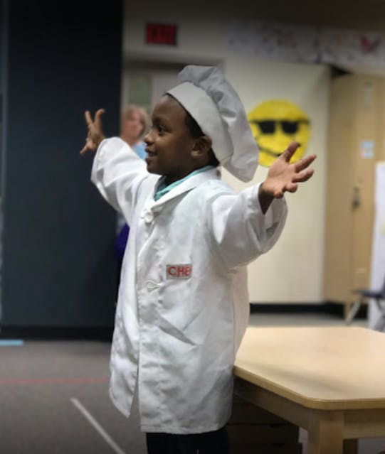 Child in a chef's hat and coat with arms outstretched