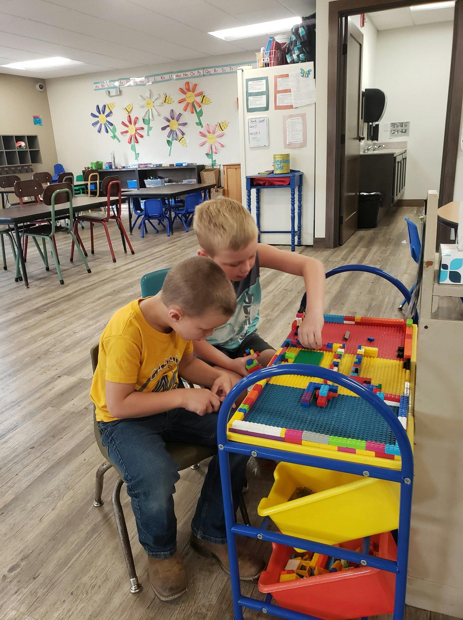 Two children playing with building blocks at a table in a classroom