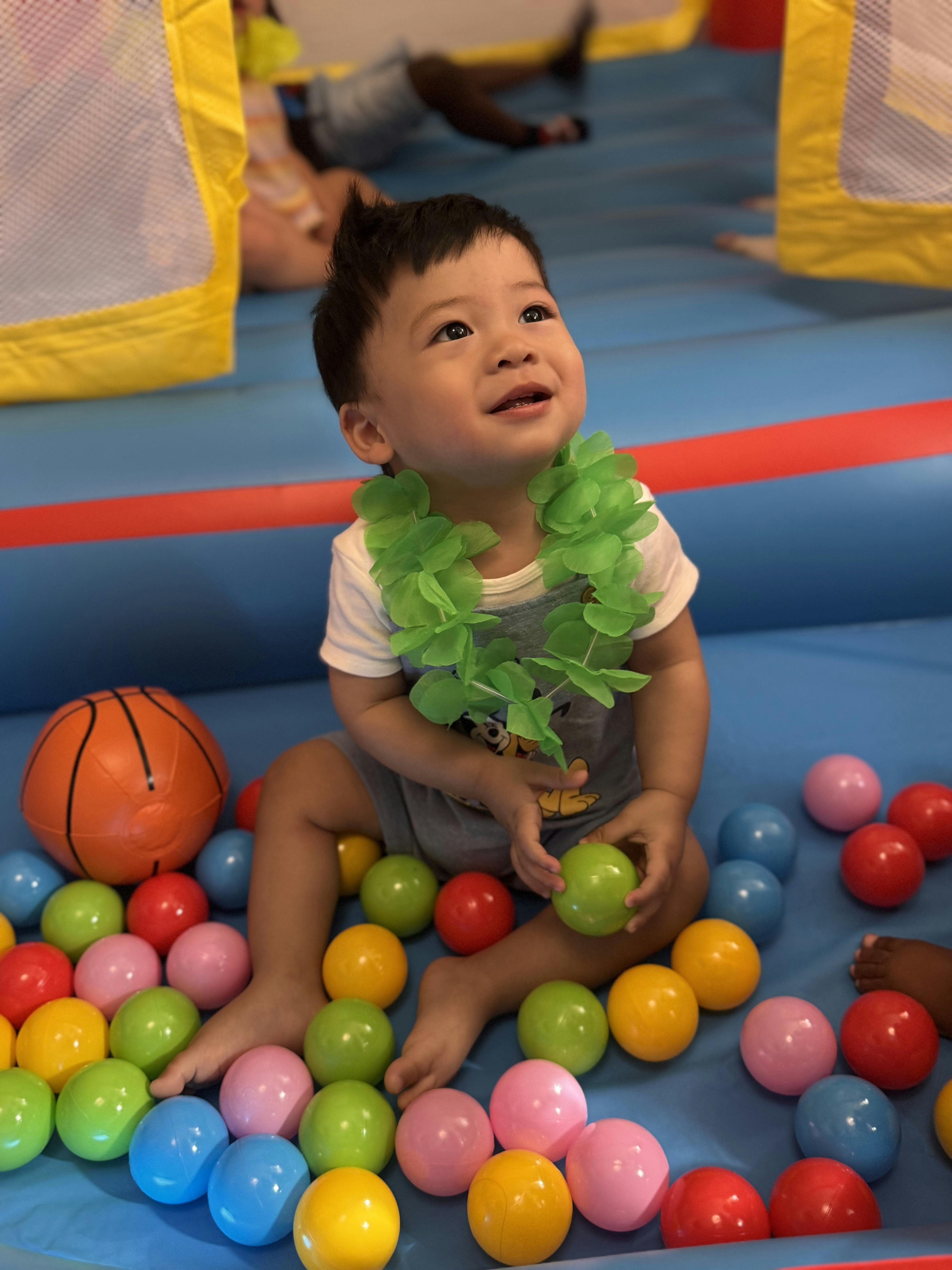 Child sitting in a ball pit wearing a green lei