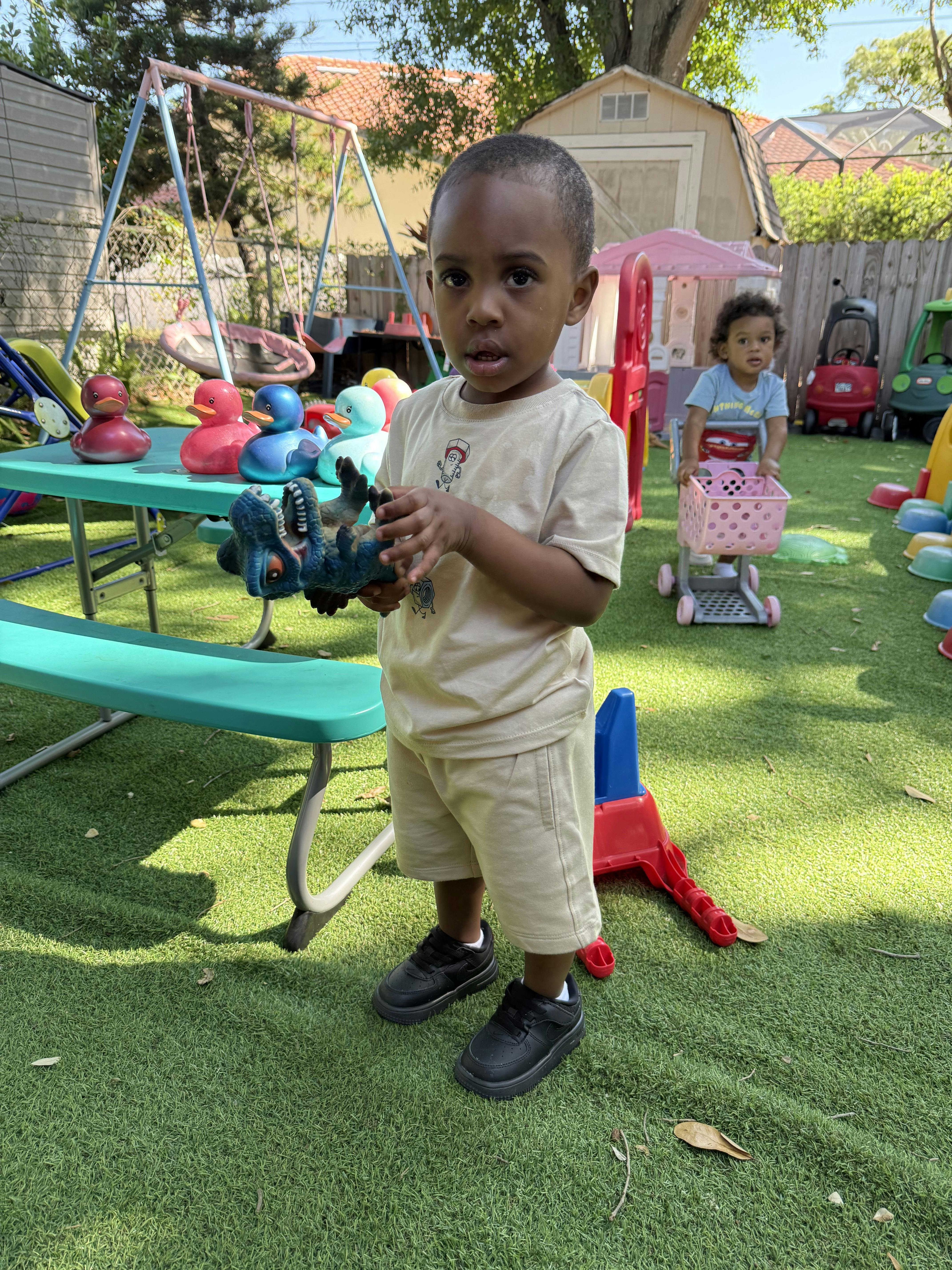 Child holding a dinosaur toy while another child pushes a shopping cart