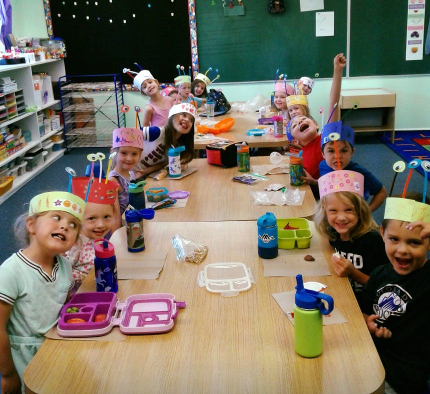 Children wearing paper hats sitting at tables in a classroom