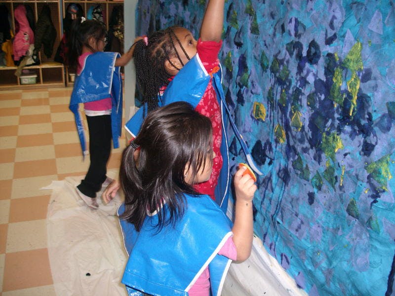 Children in smocks painting a large blue mural