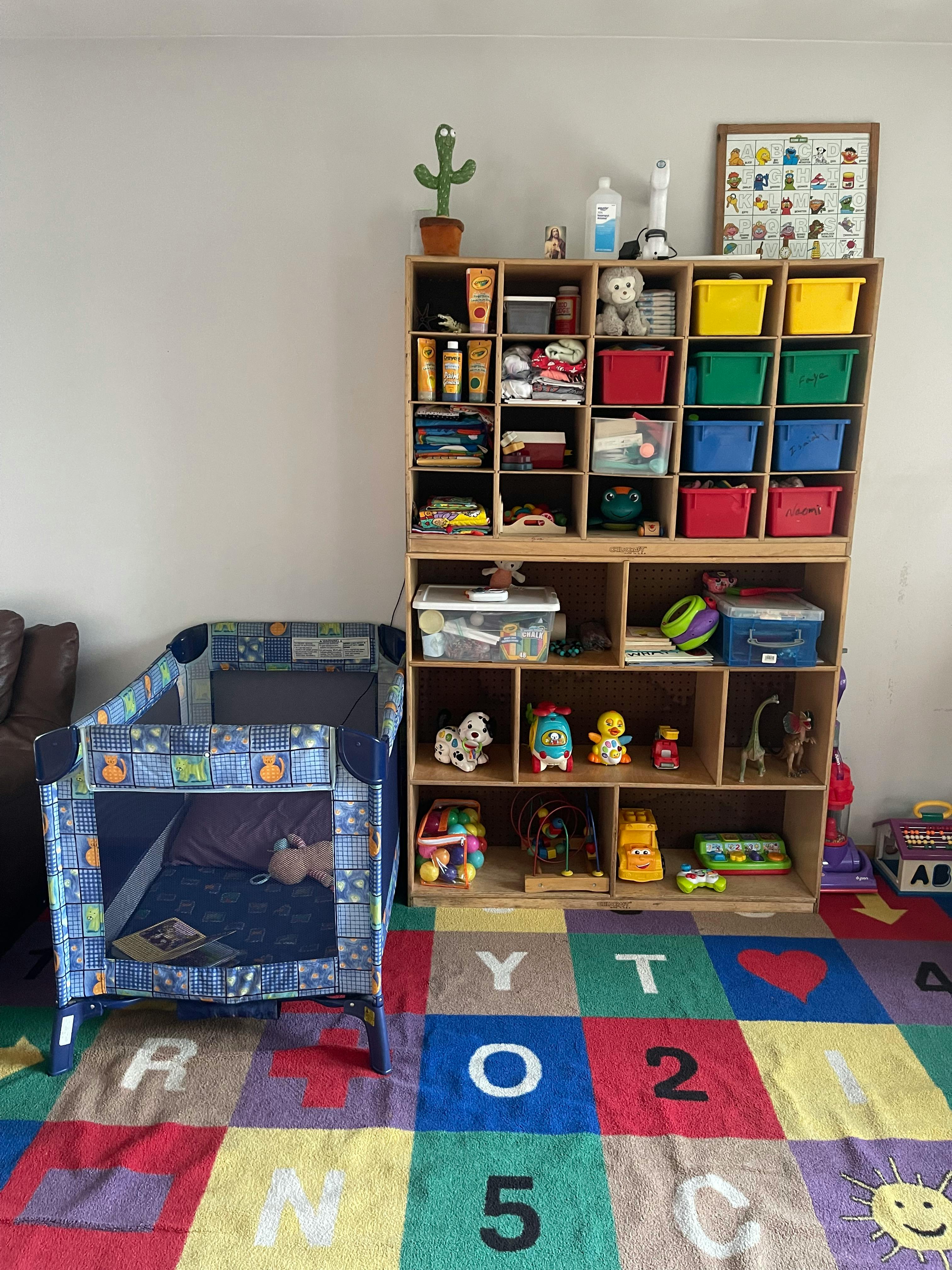 Playpen next to a wooden storage shelf with toys and bins