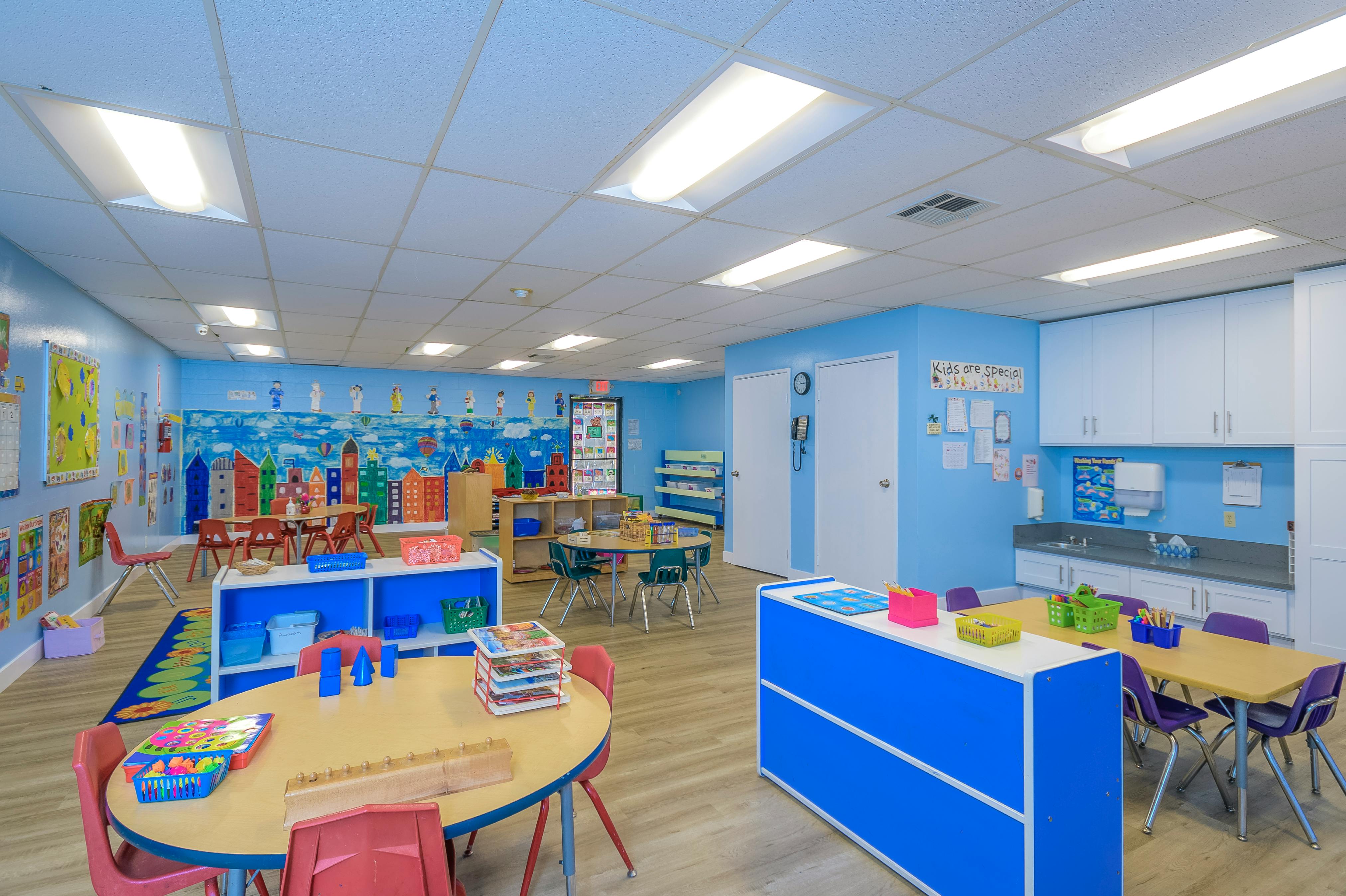 Classroom with small tables and chairs, blue walls, and a sink area
