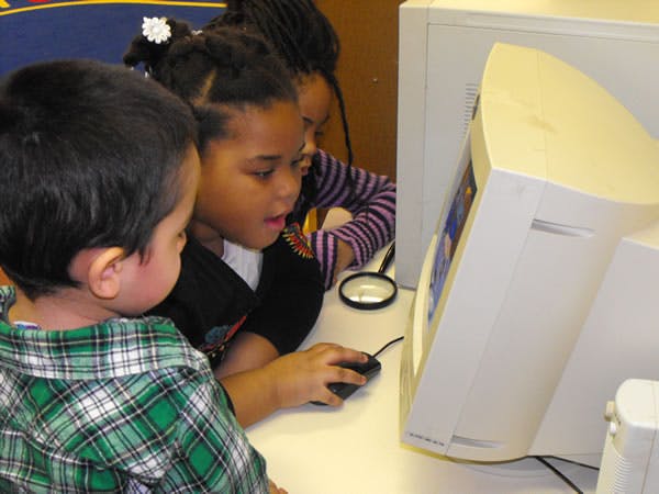 Two children looking at a computer screen, one holding a mouse