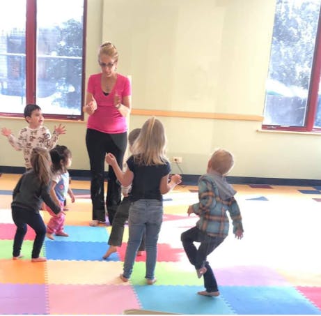 Adult person interacting with multiple children in a room with colorful floor