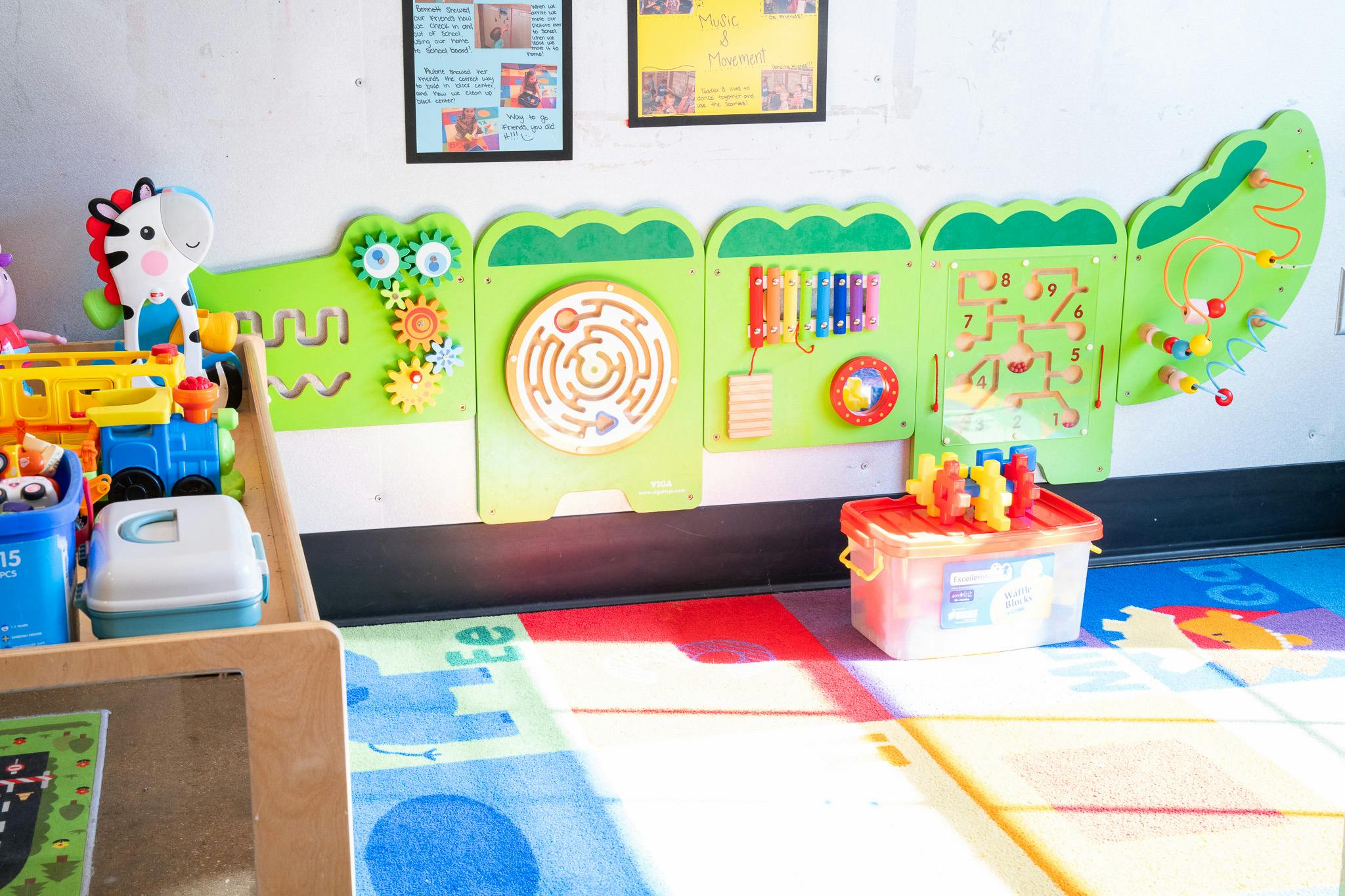 Wall-mounted activity centers in a classroom with a colorful play rug