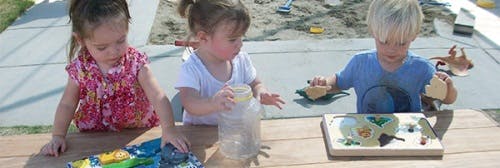 Three children playing at a table outdoors