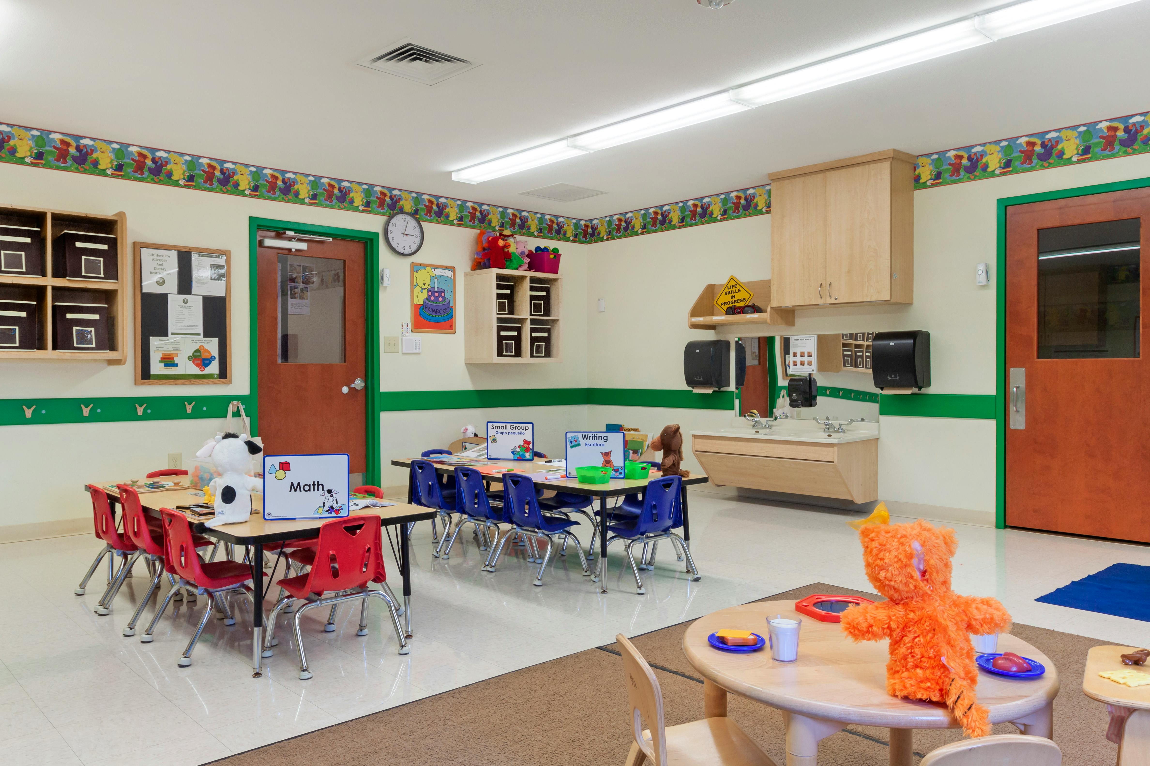 Classroom with small tables and chairs, toys, and a sink area