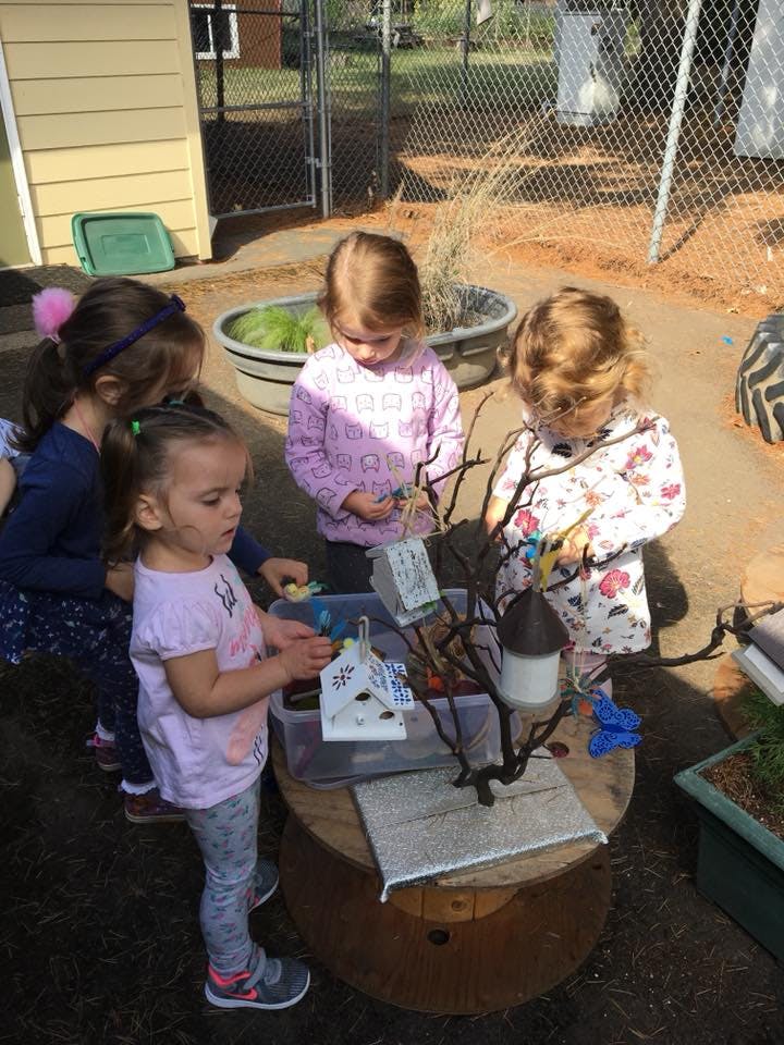 Children playing with small birdhouses and branches outdoors