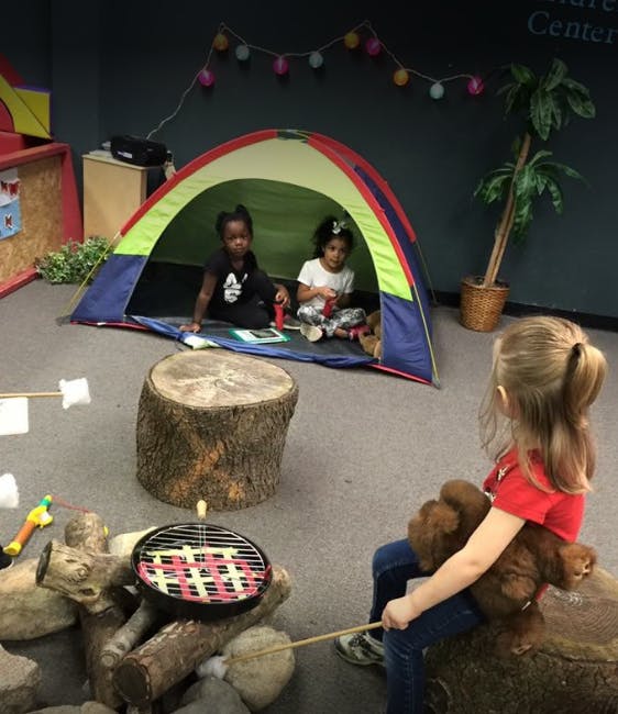 Three children playing with a tent and pretend campfire