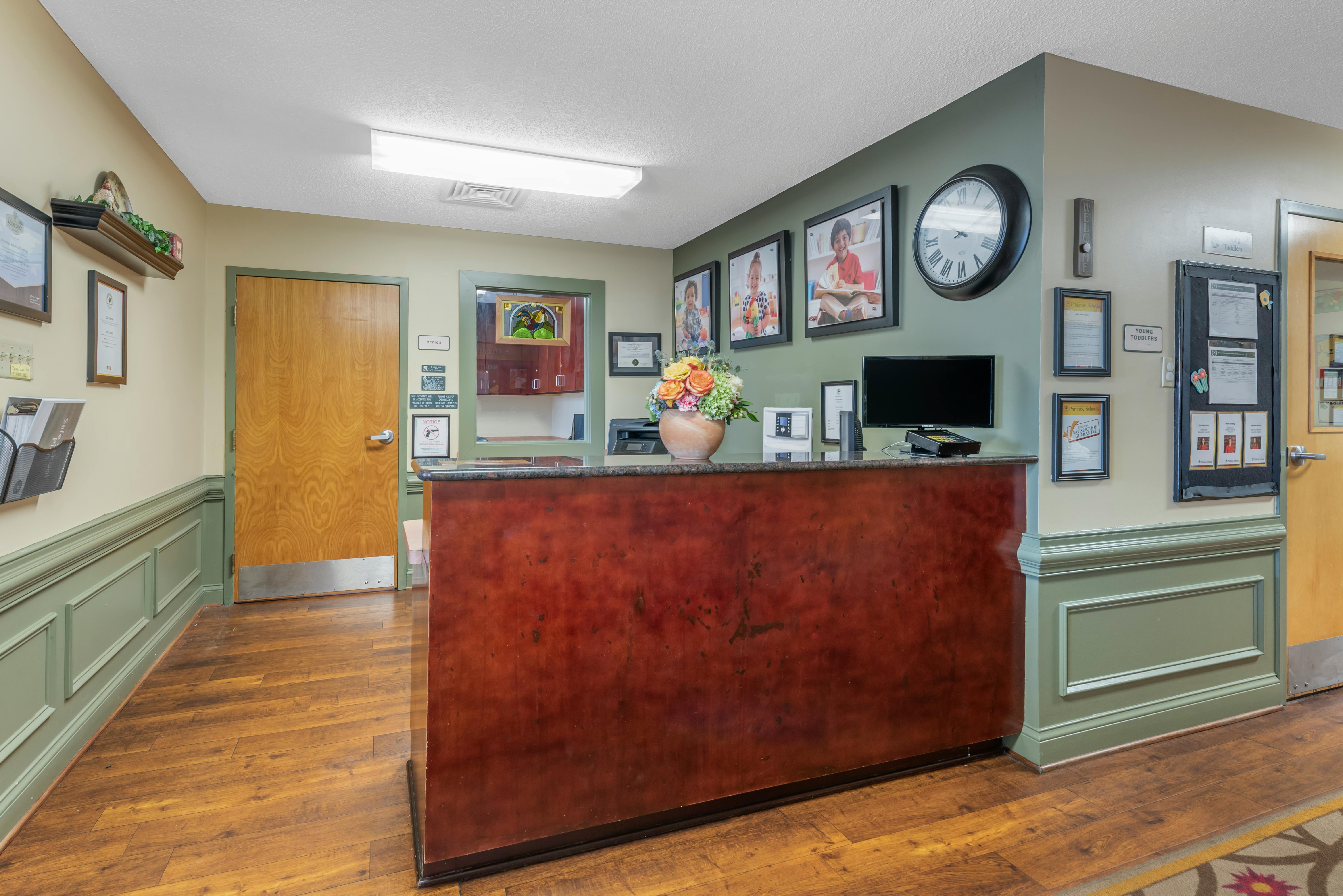 Reception area with a dark wood counter, monitor, floral arrangement, and framed pictures