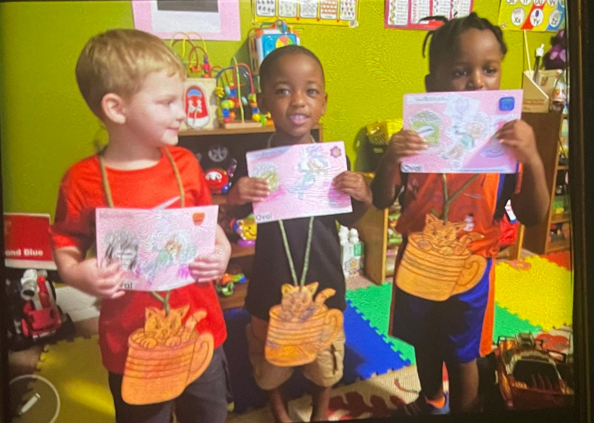 Three children holding up drawings in a classroom