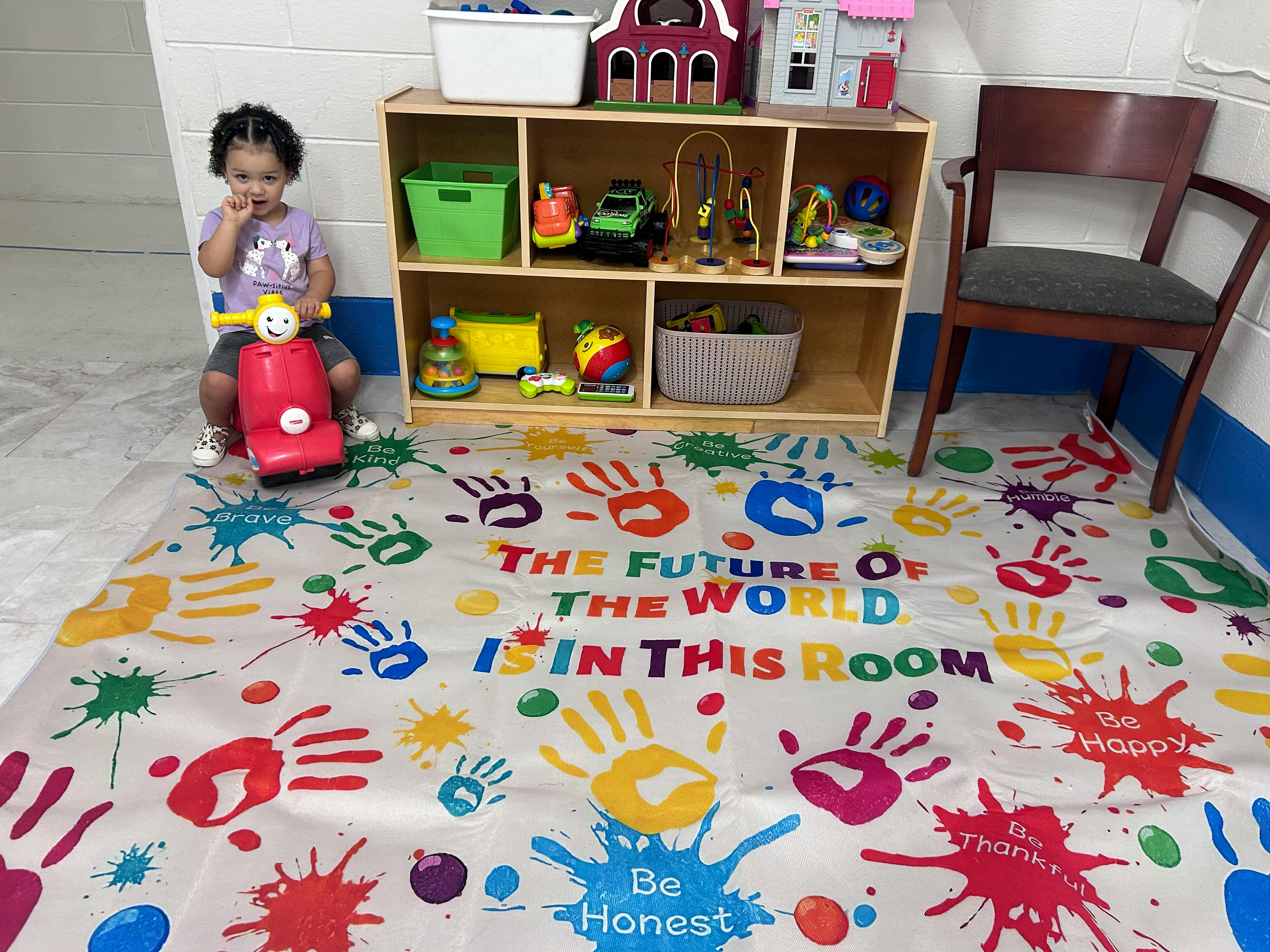 Child sitting on a red toy scooter in a room with a colorful mat