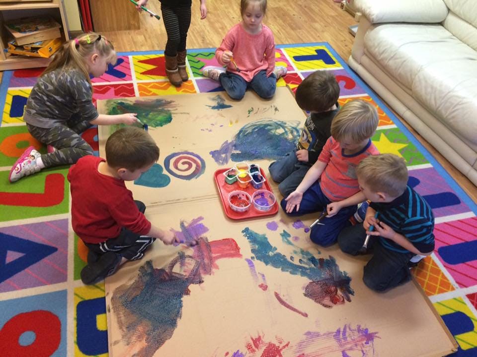 Children painting on a large sheet of paper on the floor
