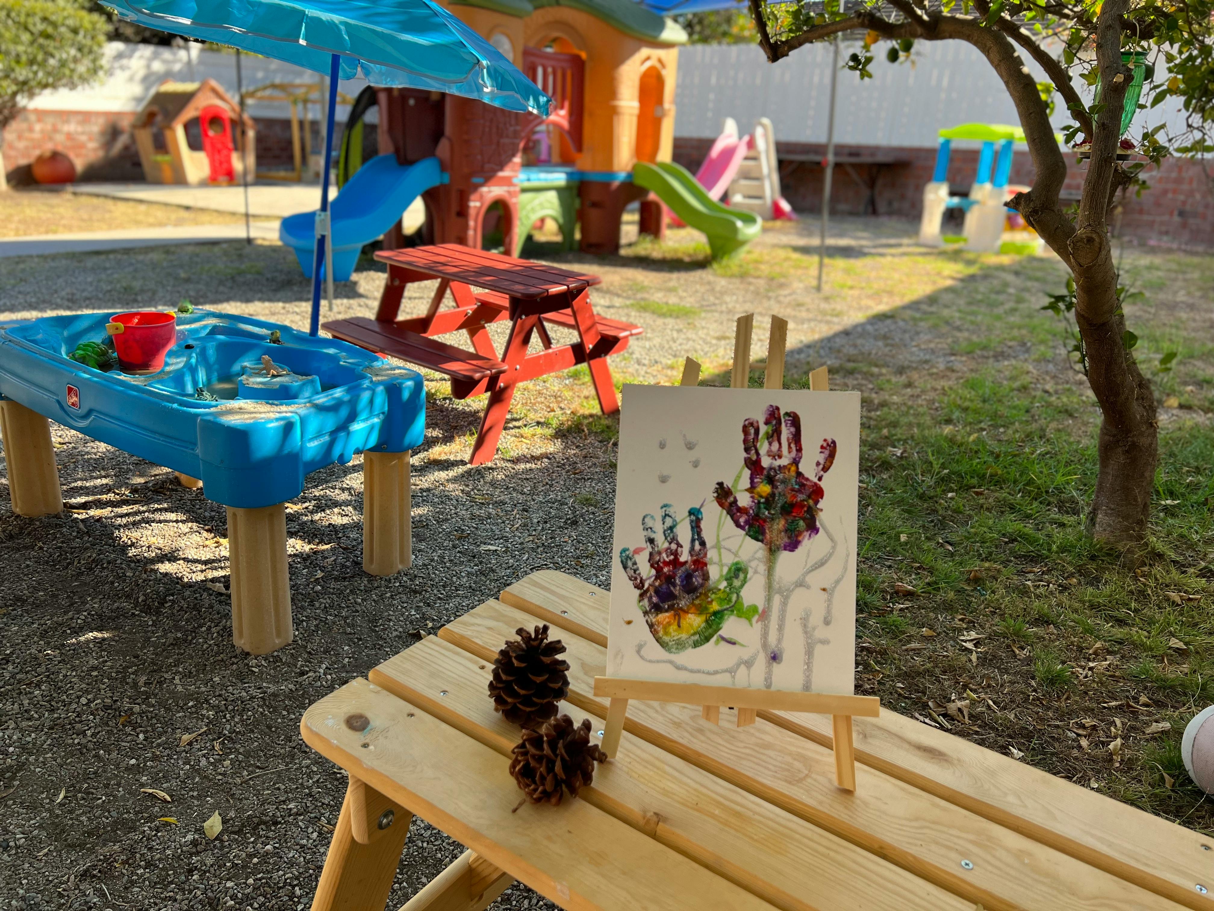 Child's handprint art on an easel with pinecones on a wooden table
