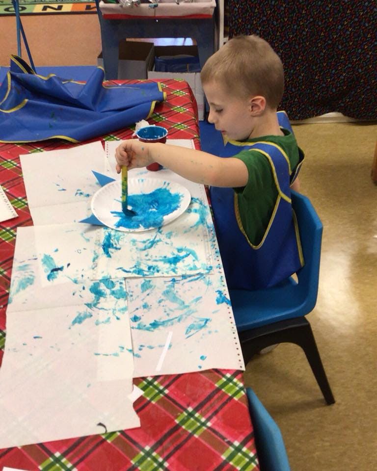 Child painting with blue paint on a paper plate