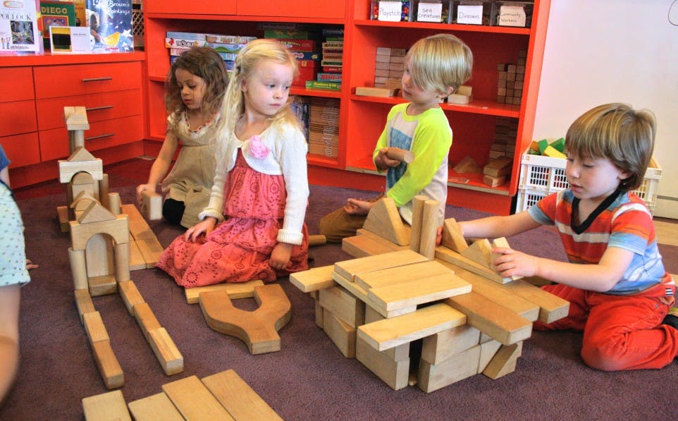 Four children playing with wooden blocks on a floor