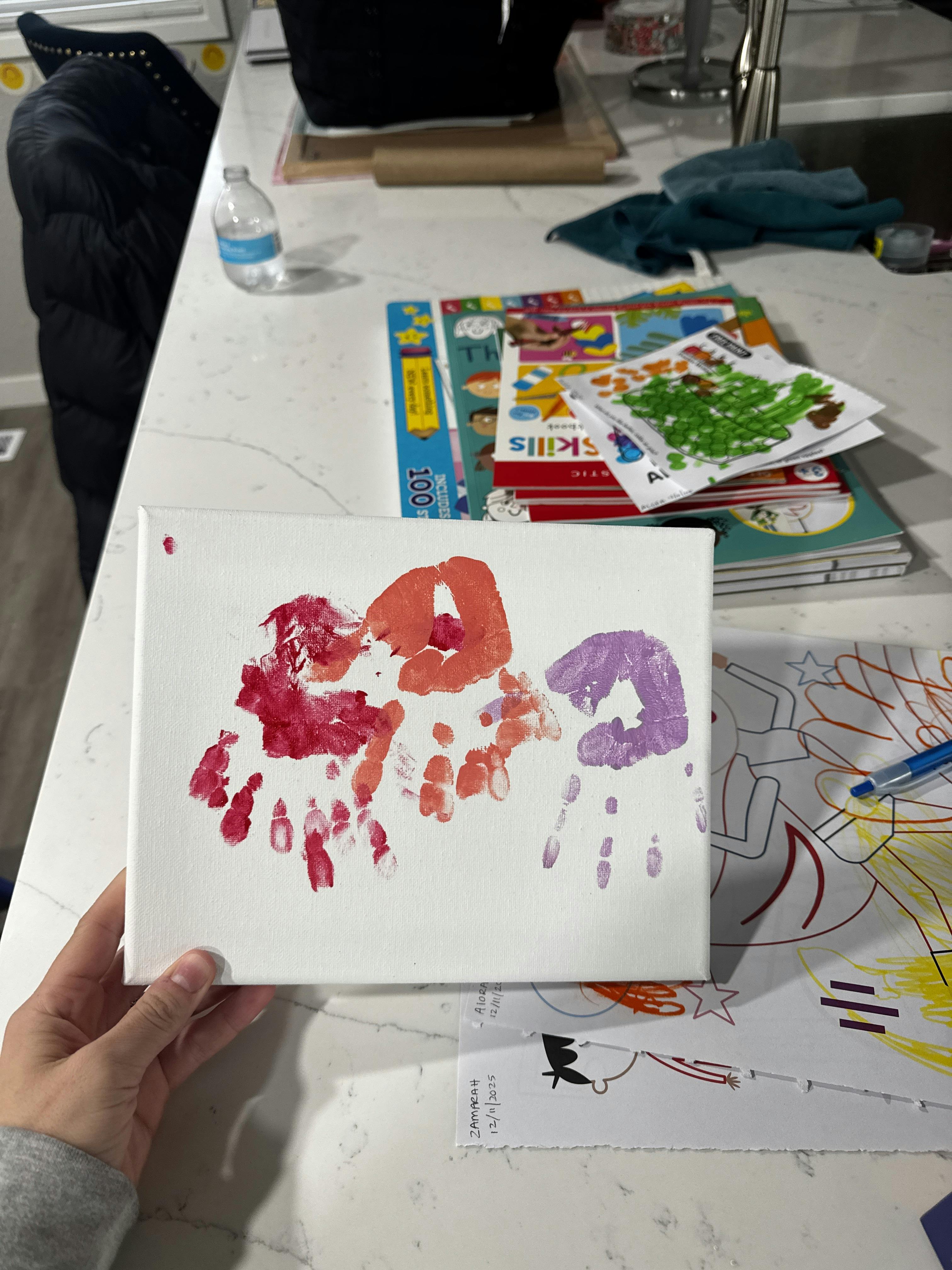Person holding a canvas with red, orange, and purple handprints