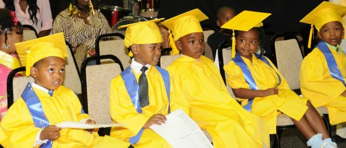 Children in yellow graduation caps and gowns sitting in chairs