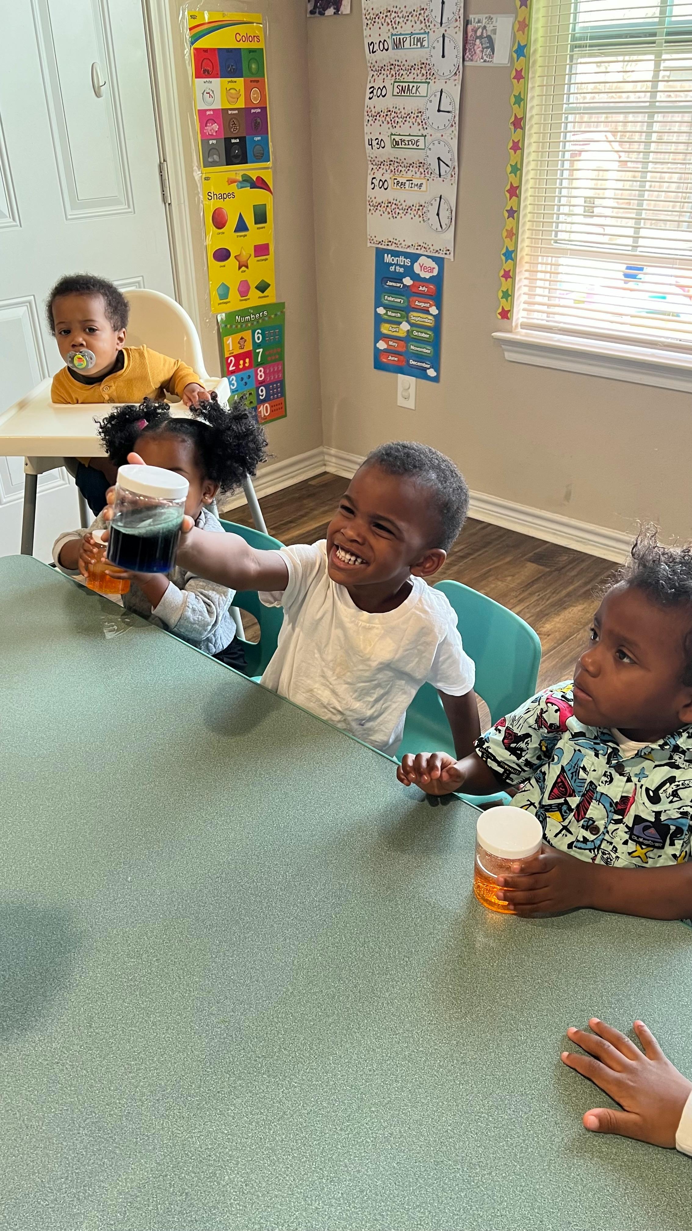 Children sitting at a table, one holding up a jar
