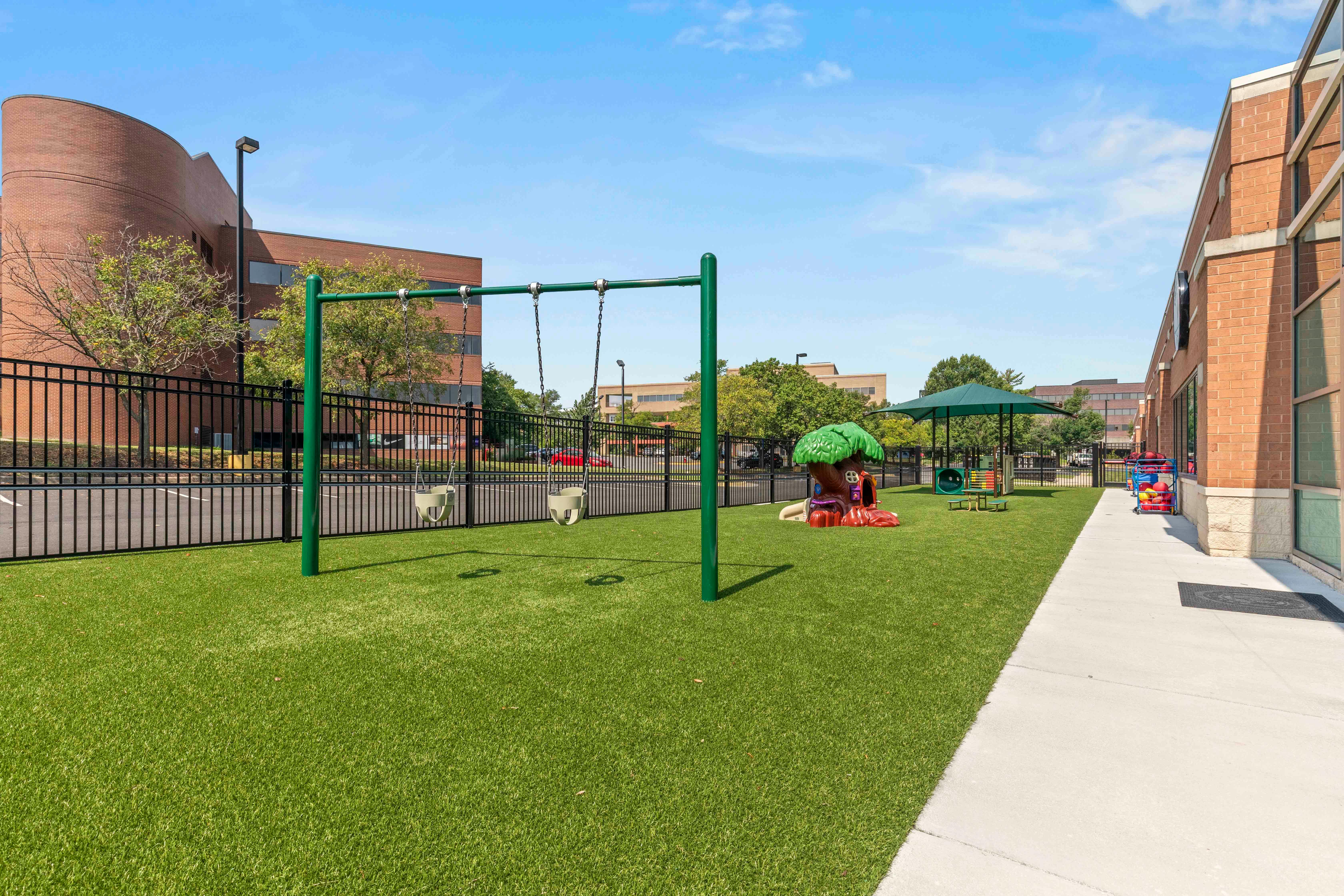 Outdoor playground with green swings, a tree-shaped play structure, and green turf
