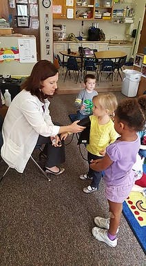 Person in white coat checking a child's arm, two other children nearby