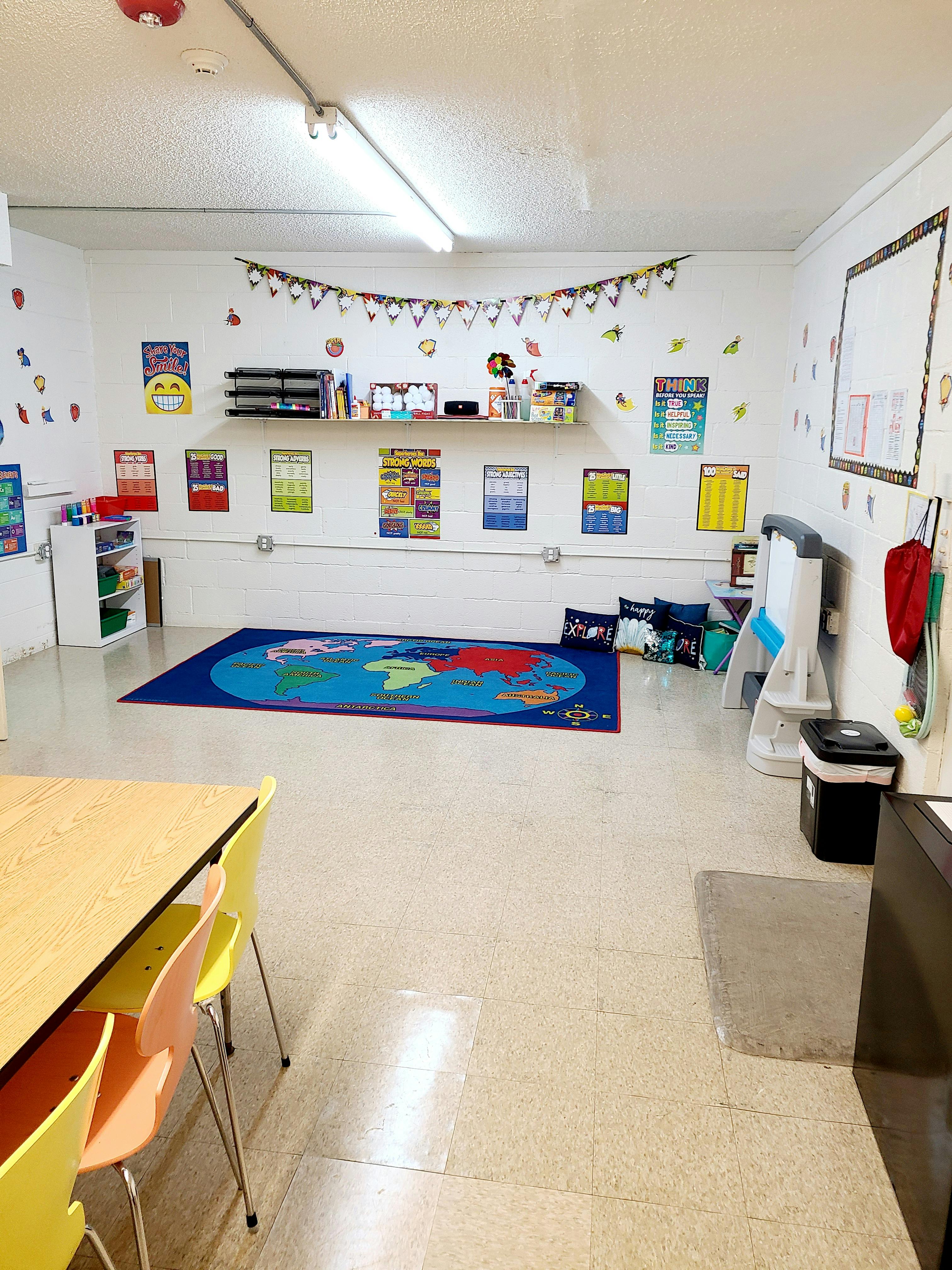 Classroom with a world map rug, posters on the wall, and tables with chairs