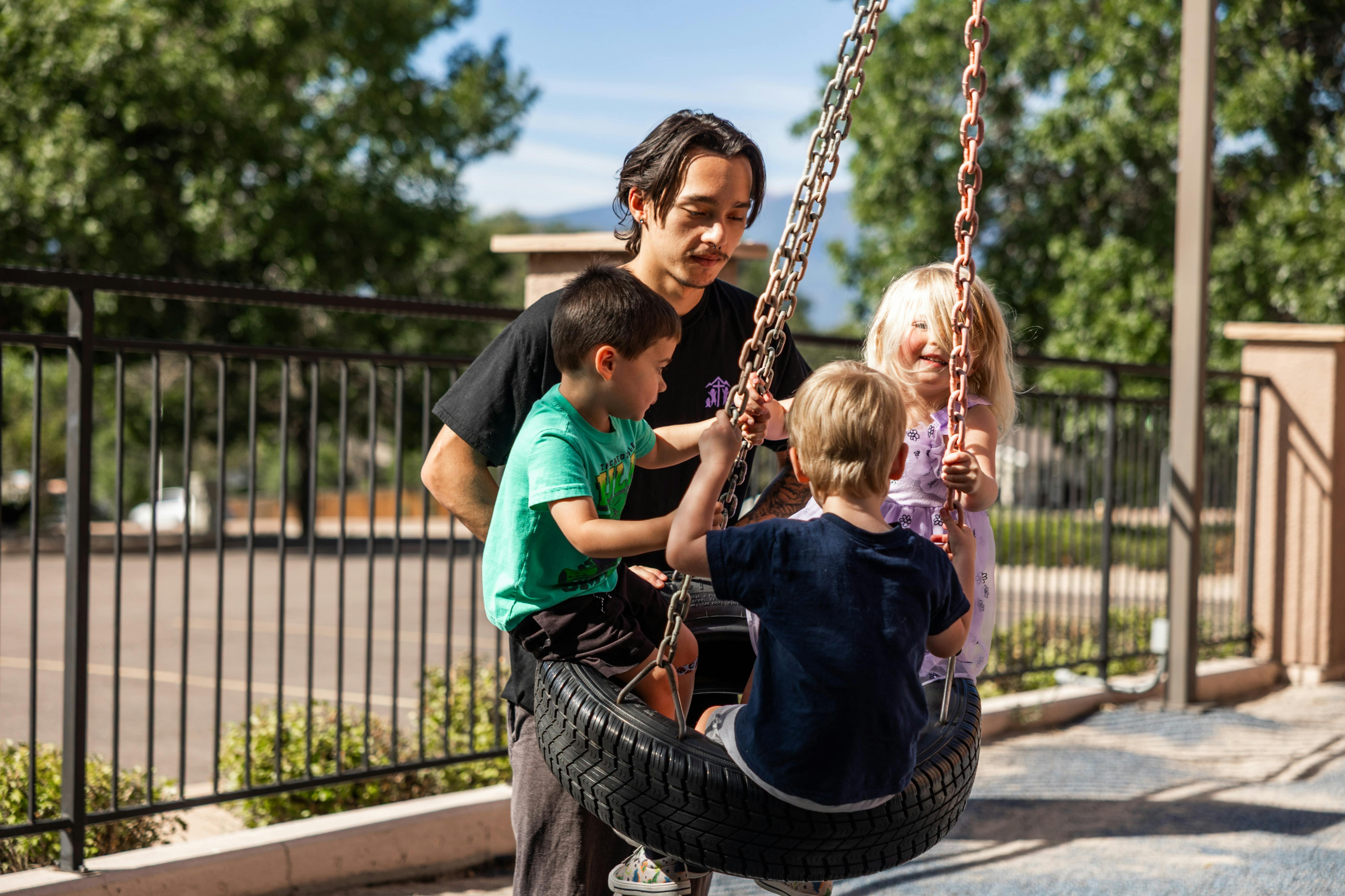 Person helping three children on a tire swing