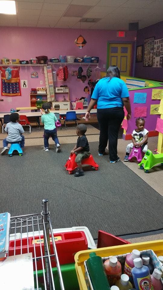 Adult supervising children playing on ride-on toys in a classroom