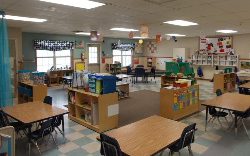 Empty classroom with tables, chairs, and shelves of educational materials