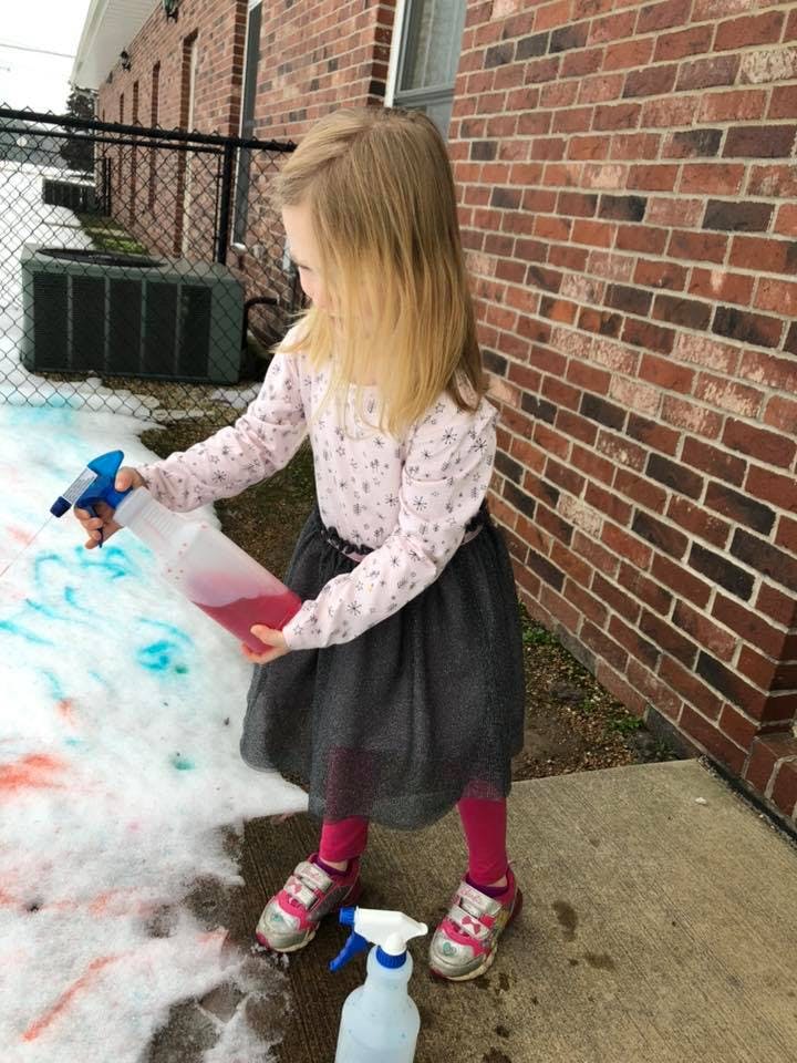 Child spraying colored liquid onto snow
