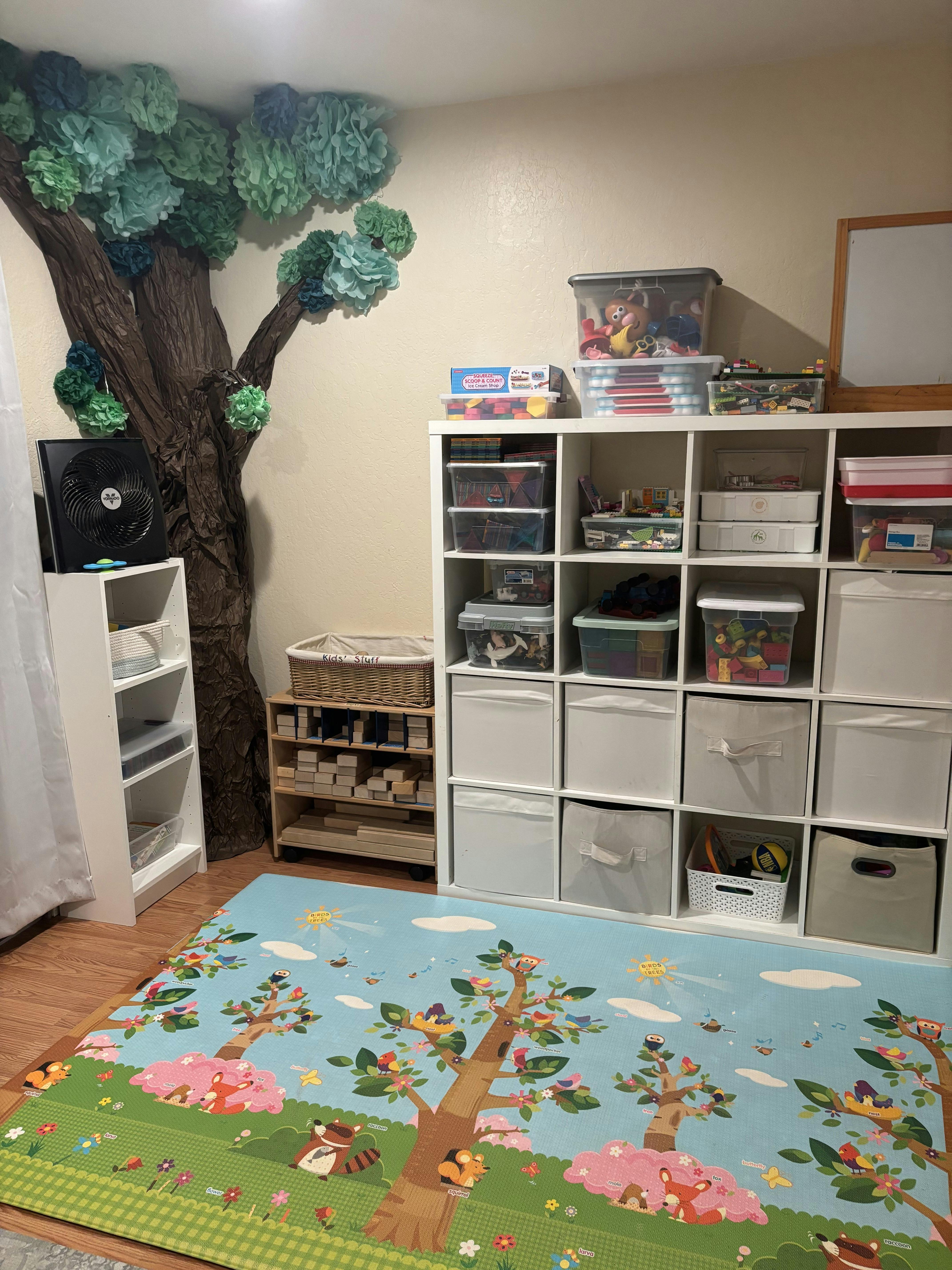 Playroom with a tree decoration, storage shelves, and a colorful play mat