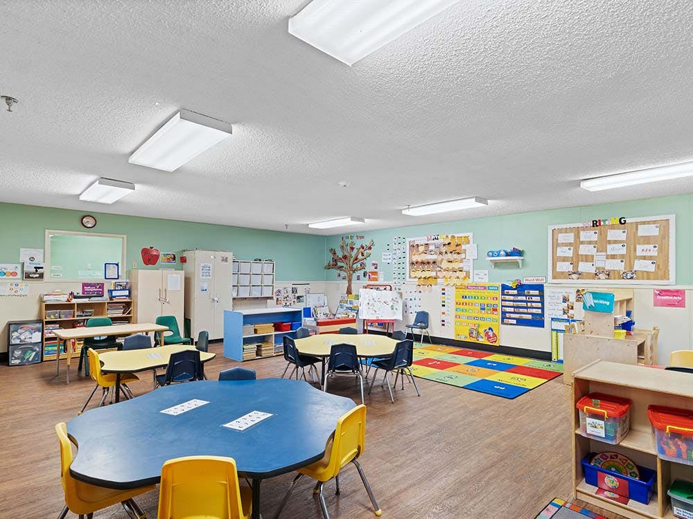 A classroom with small tables and chairs, toys, and decorations on the walls