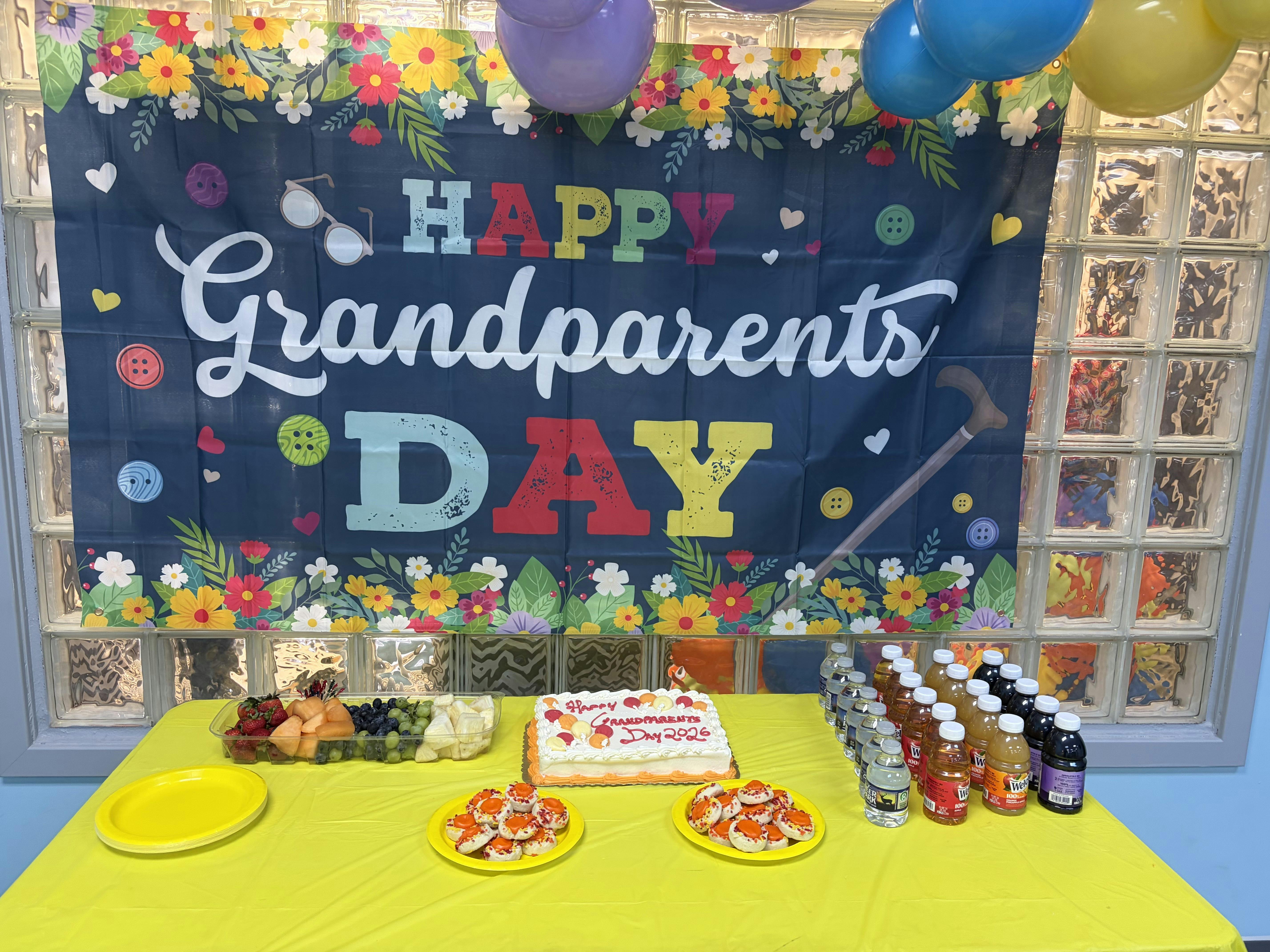 Grandparents Day party banner with refreshments and cake on a yellow table