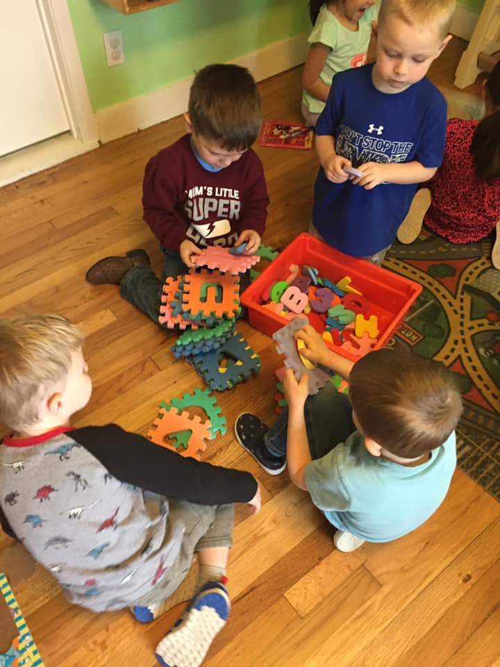 Children playing with foam letters and shapes on a wooden floor
