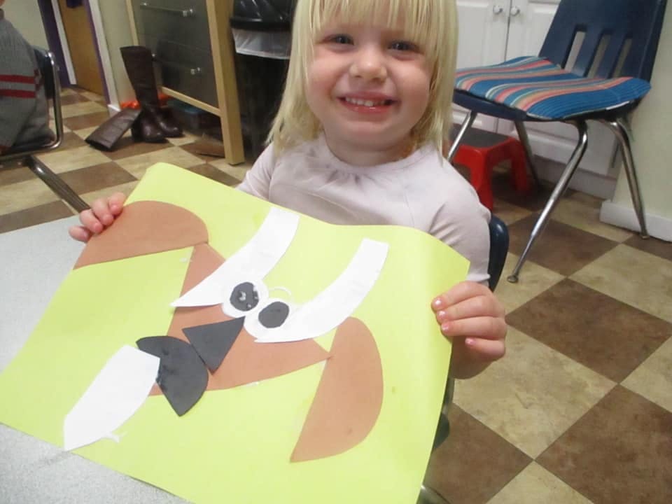 Child holding up a paper craft with cut-out shapes