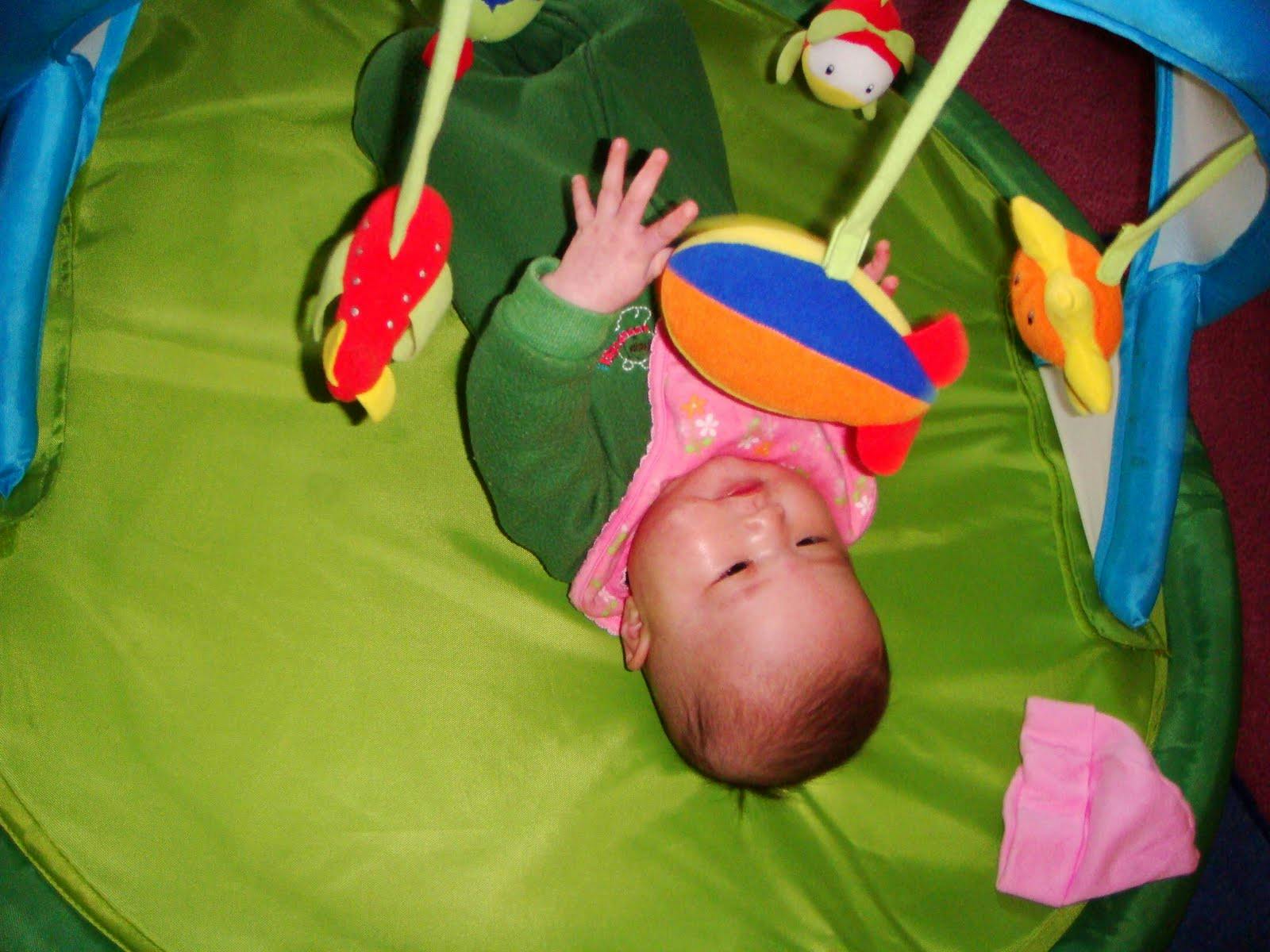 Child playing with hanging toys on a green mat