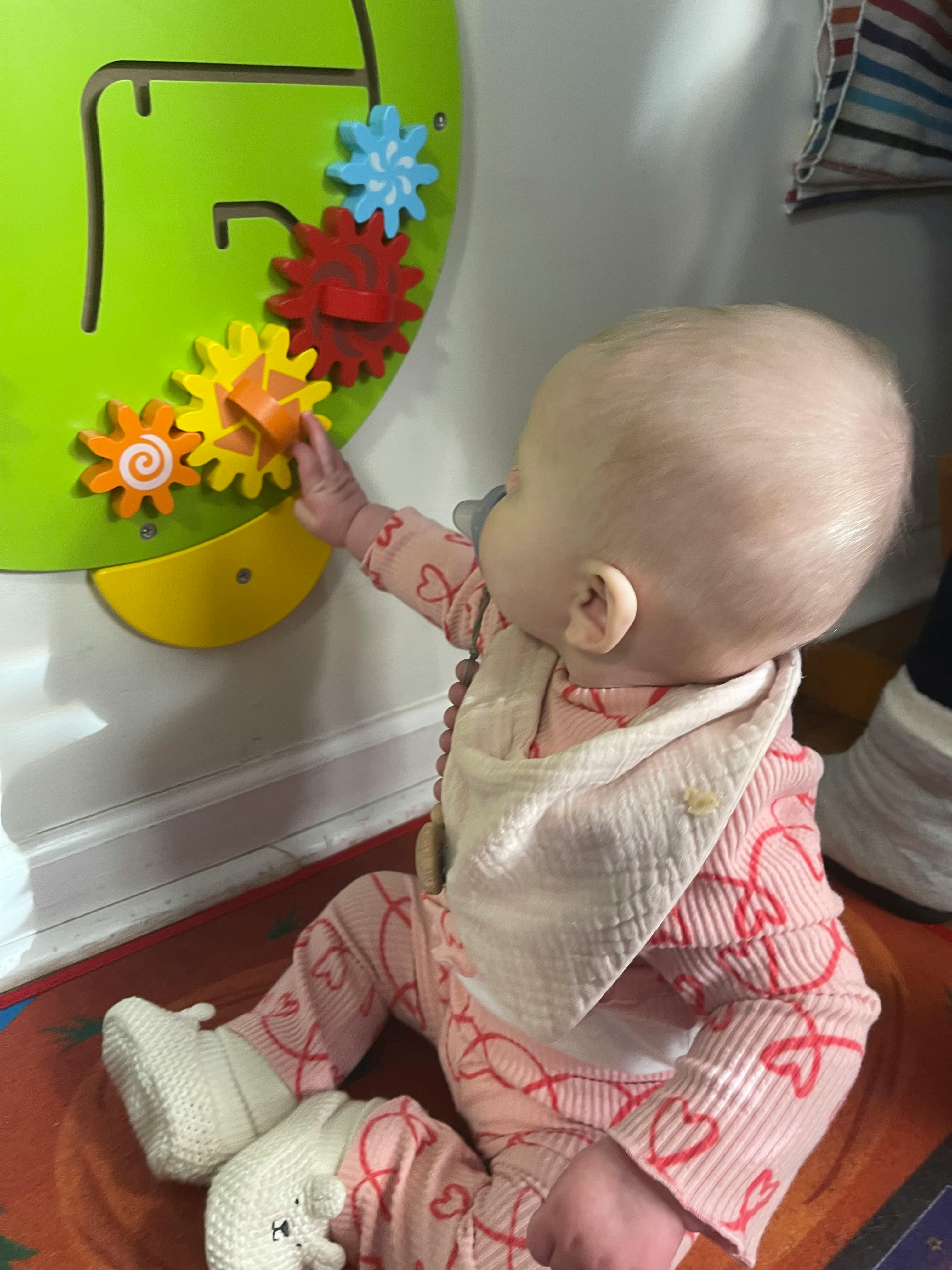 Child playing with colorful gears on a green activity board