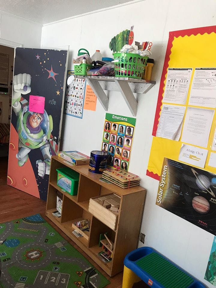 Classroom corner with a Buzz Lightyear cutout, shelves, and educational posters
