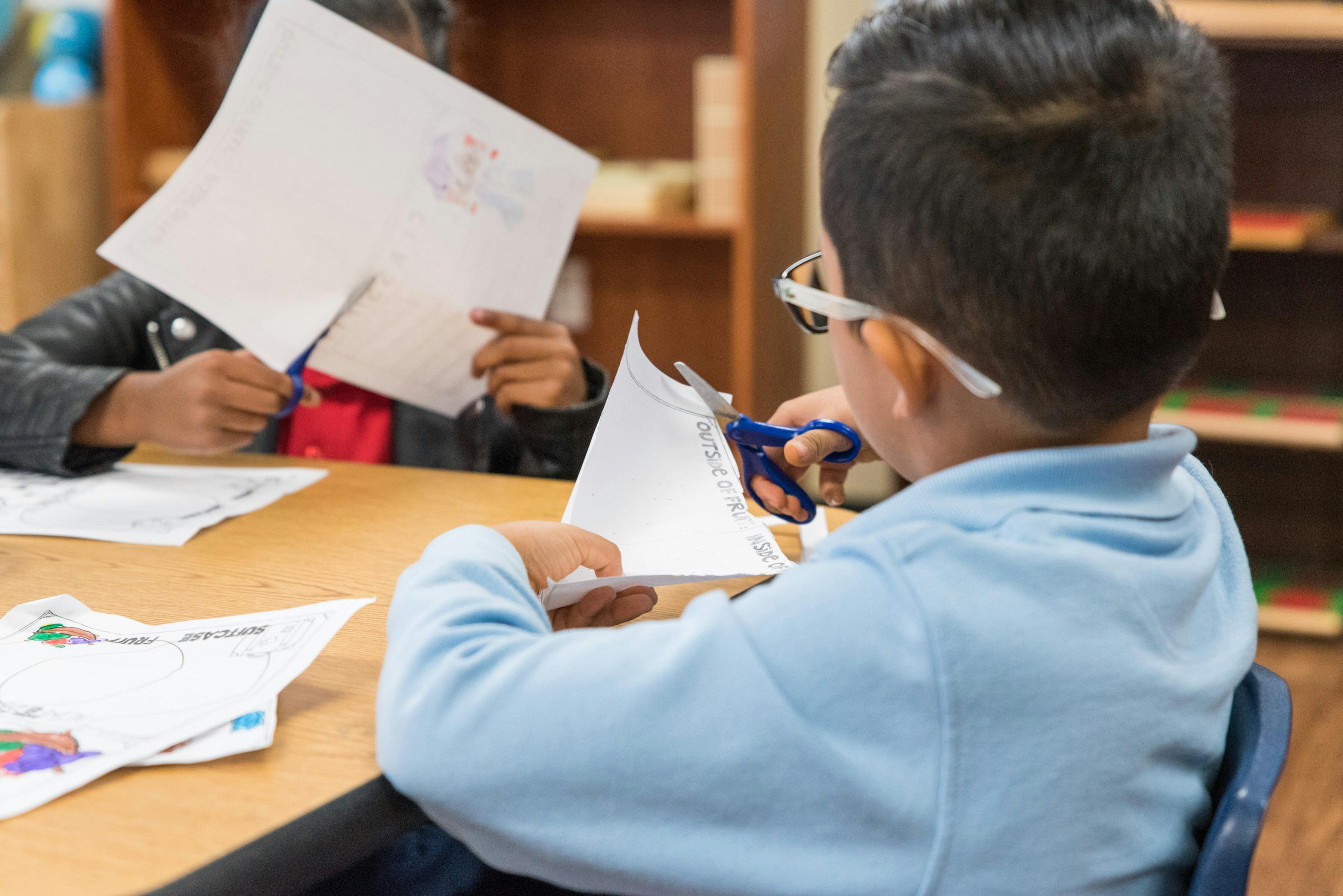 Two children cutting paper with scissors at a table