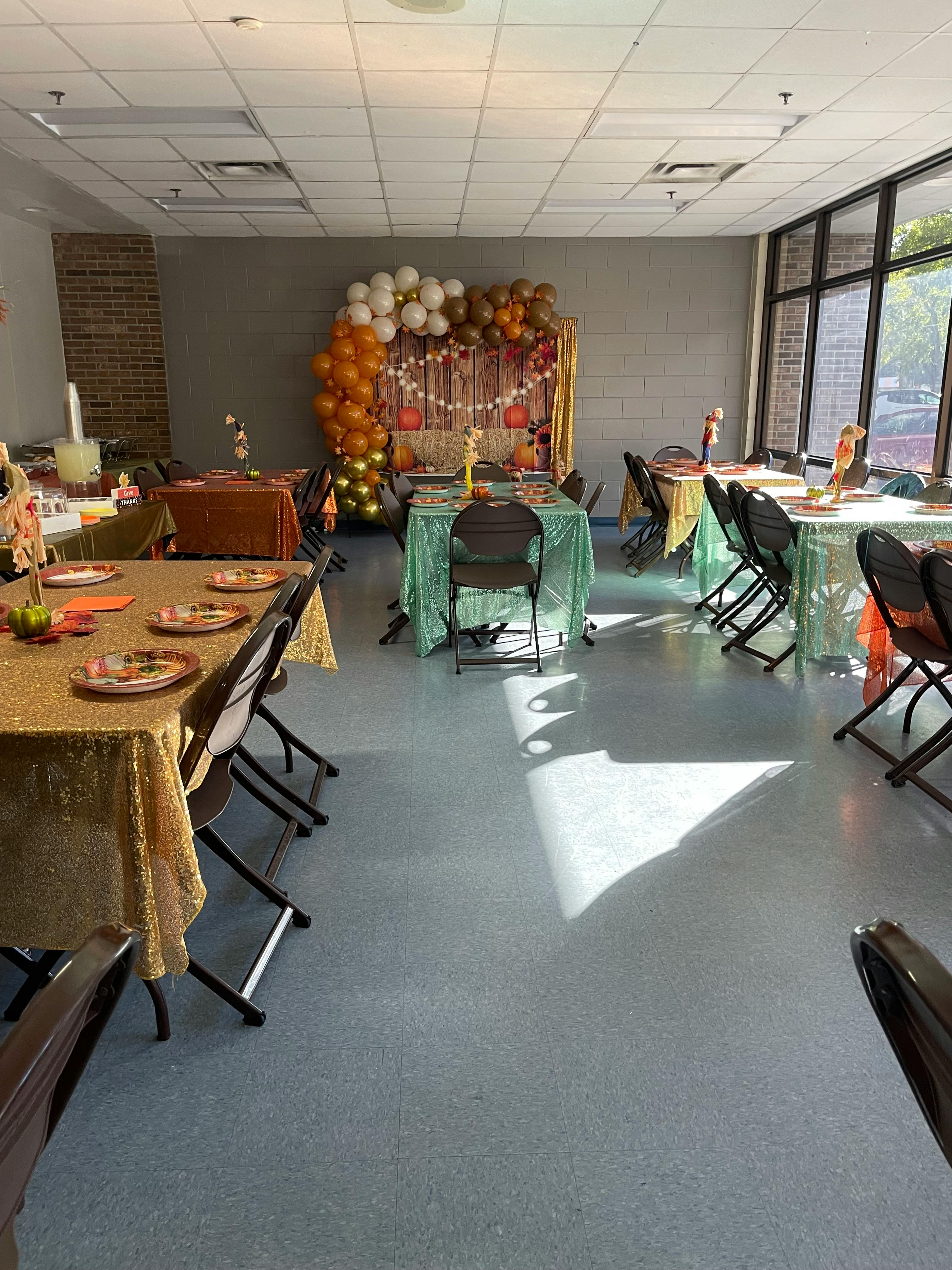 Room with tables and chairs set up for an event, balloon arch in background