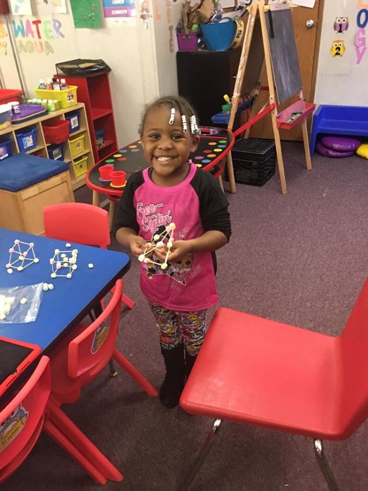 Child holding a geometric shape made from marshmallows and toothpicks