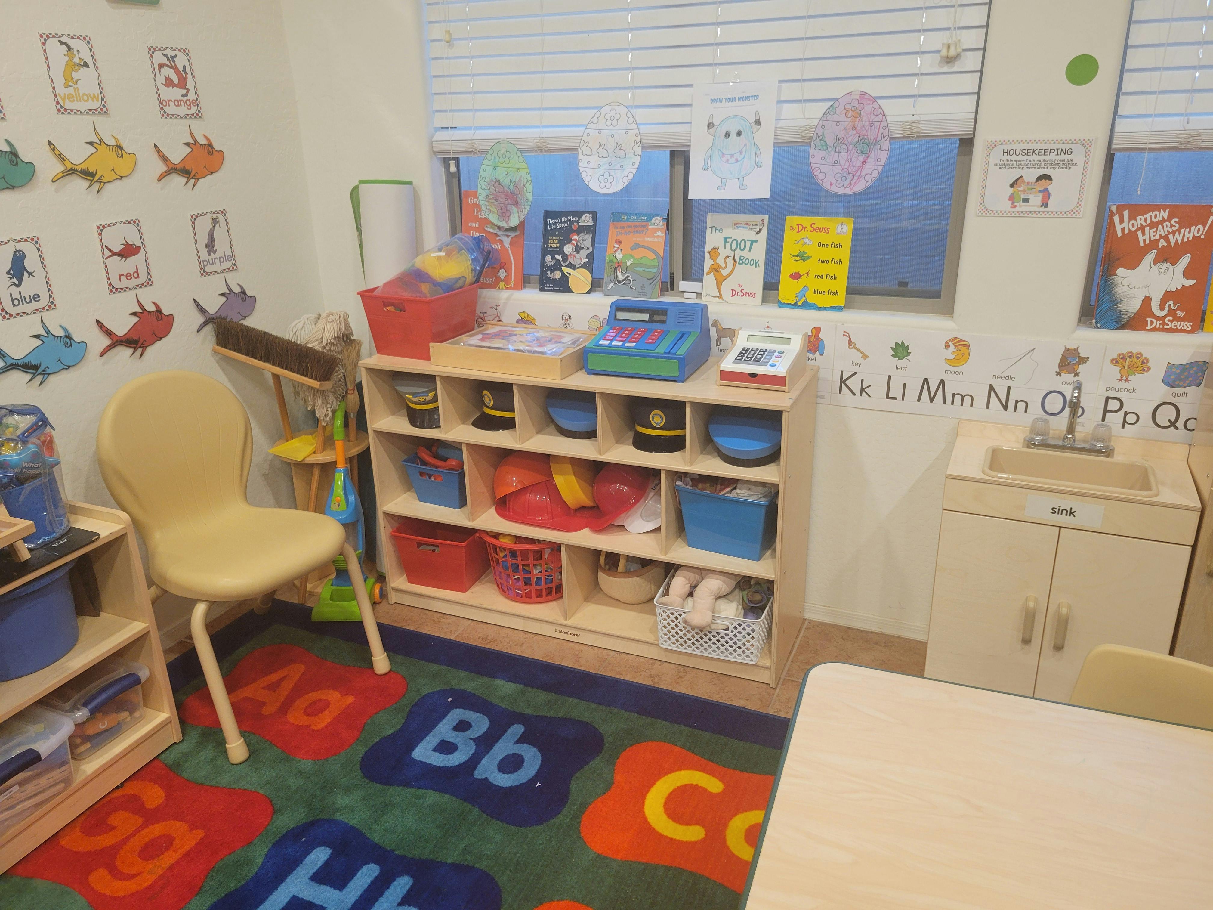 Classroom with a colorful alphabet rug, shelves with toys, and a play sink