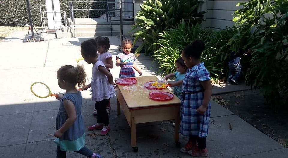 Children playing with plates at a table outdoors