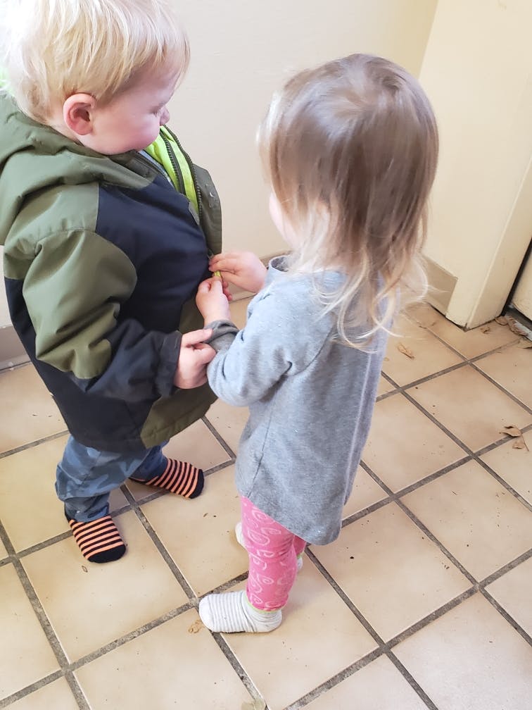 Child helping another child with a jacket zipper