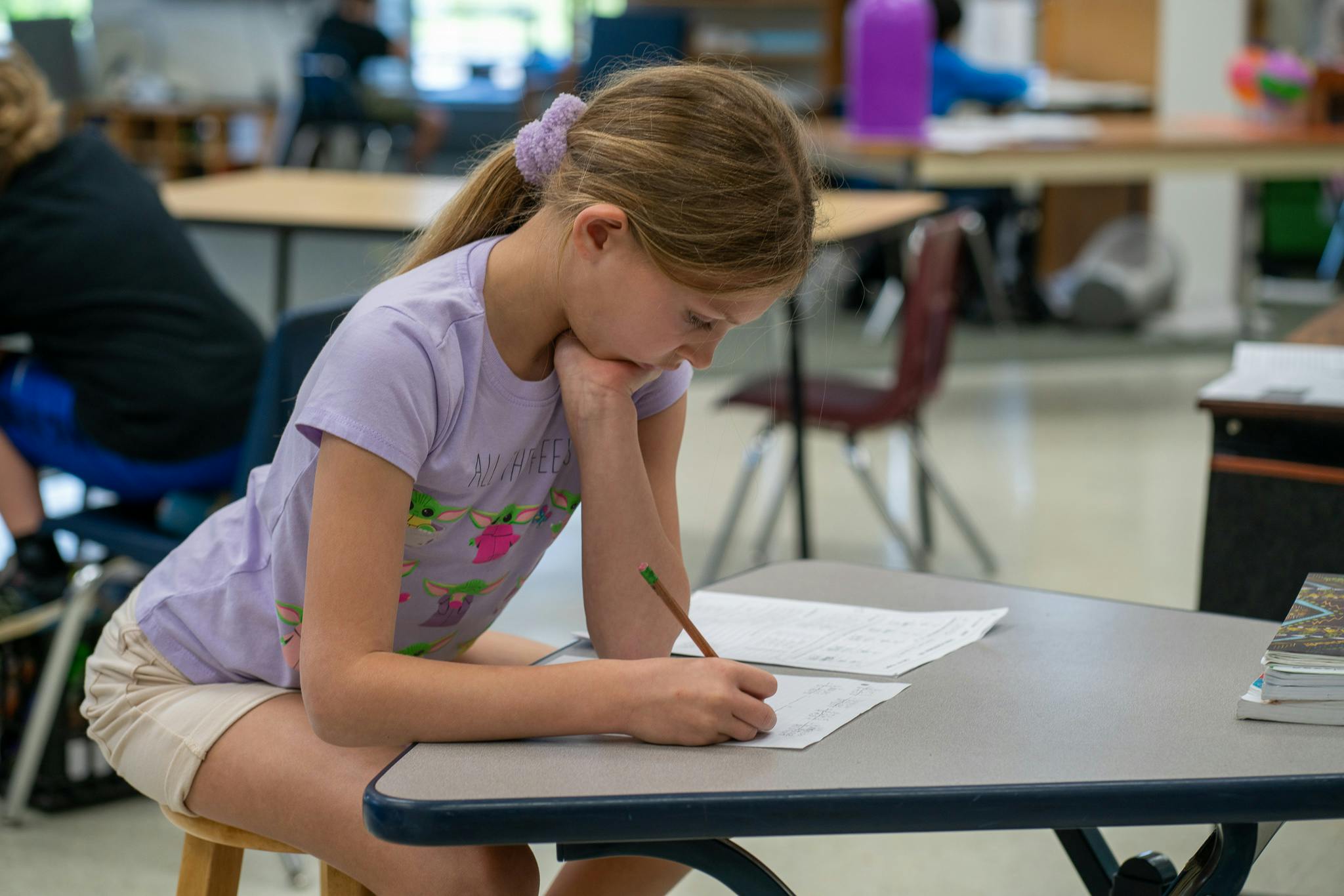 Child writing on paper at a desk in a classroom