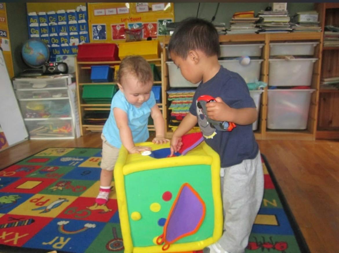 Two children playing with a large foam activity cube in a classroom