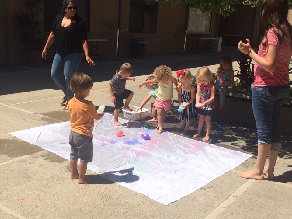 Children and adults painting on a large white sheet outdoors