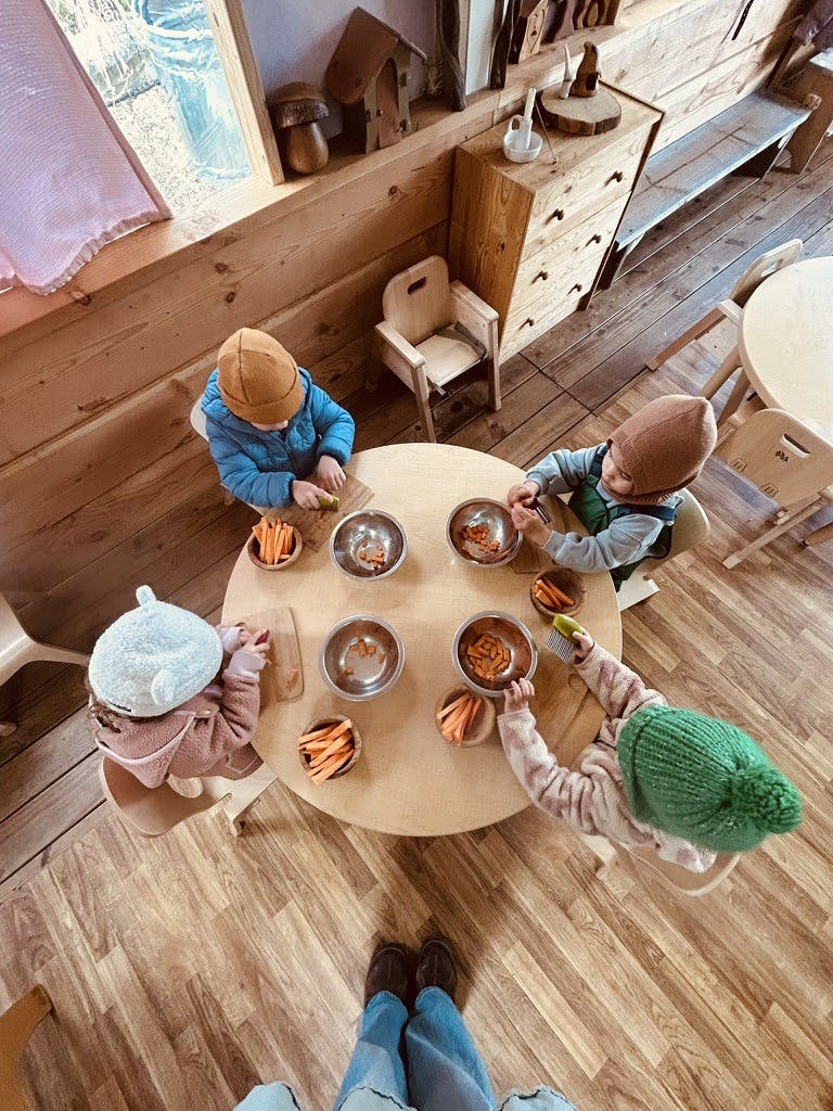 Four children sitting at a round table preparing carrots